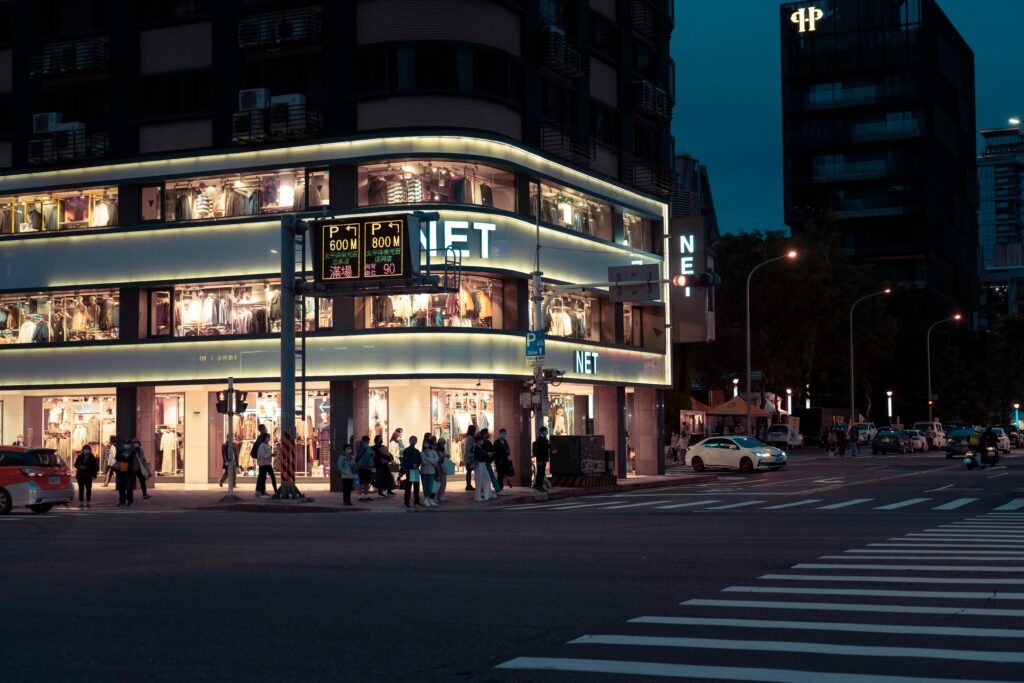 Dynamic night shot of a city street with an illuminated clothing store and bustling pedestrian activity.